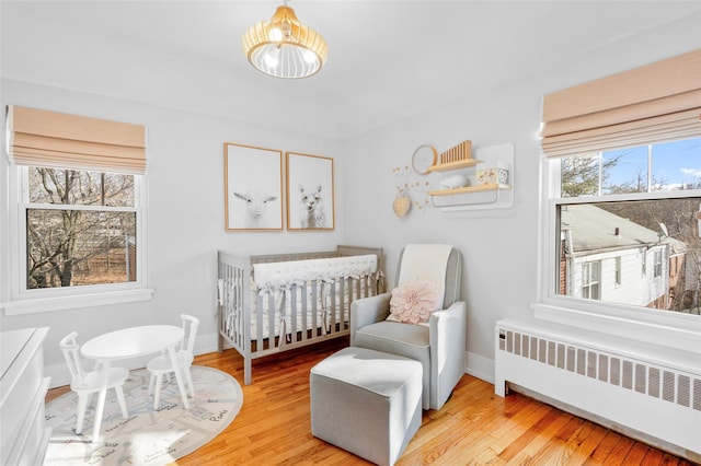 bedroom with a crib, radiator heating unit, and light hardwood / wood-style flooring