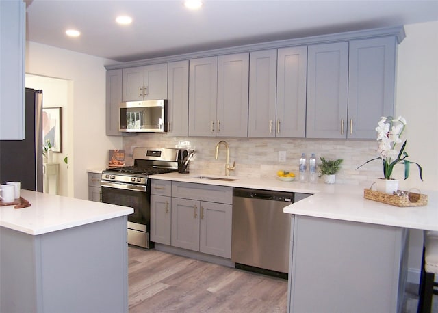 kitchen with sink, gray cabinetry, light hardwood / wood-style flooring, appliances with stainless steel finishes, and backsplash