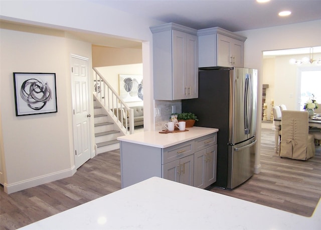 kitchen featuring gray cabinetry, stainless steel fridge, decorative backsplash, dark wood-type flooring, and an inviting chandelier