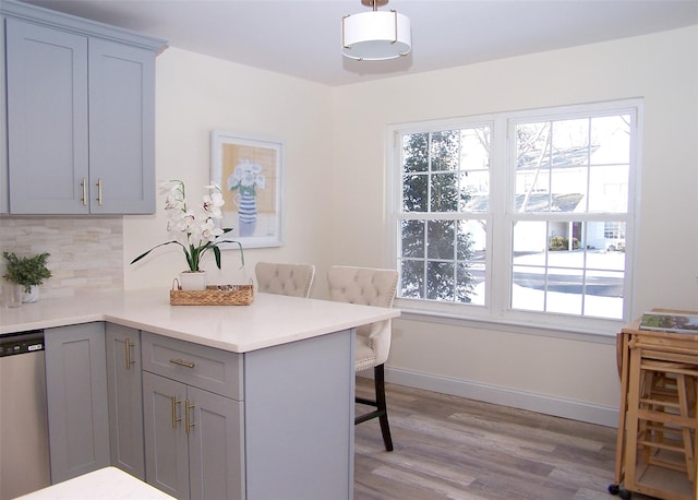 kitchen with gray cabinets, a breakfast bar, pendant lighting, tasteful backsplash, and dishwasher