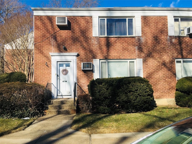 view of front facade featuring a wall mounted air conditioner and a front lawn