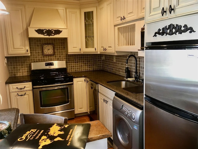 kitchen featuring washer / dryer, sink, tasteful backsplash, appliances with stainless steel finishes, and custom range hood