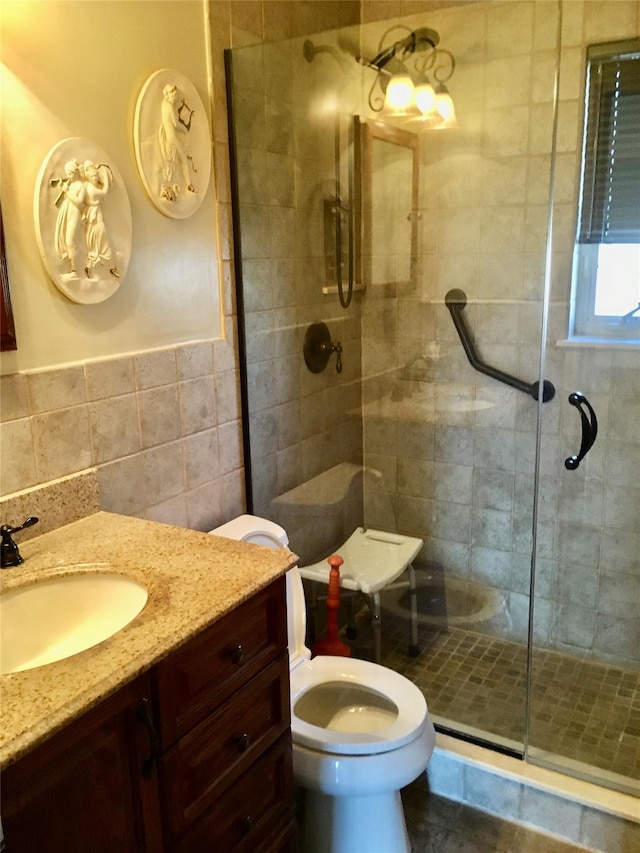 bathroom featuring a shower with door, vanity, tile walls, and toilet