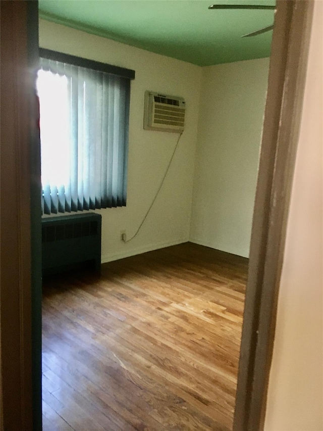 unfurnished room featuring radiator heating unit, a wall unit AC, and wood-type flooring