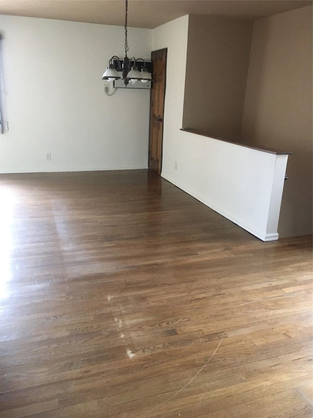 empty room featuring dark wood-type flooring and an inviting chandelier