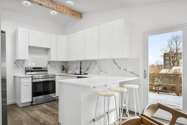 kitchen featuring sink, stainless steel electric range oven, white cabinets, a kitchen bar, and kitchen peninsula