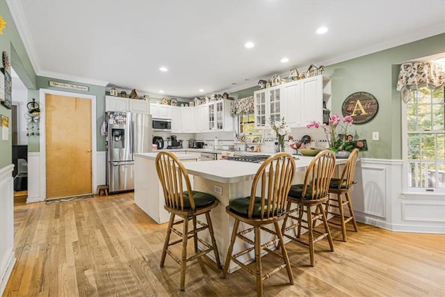 kitchen with a breakfast bar, appliances with stainless steel finishes, white cabinetry, kitchen peninsula, and light wood-type flooring