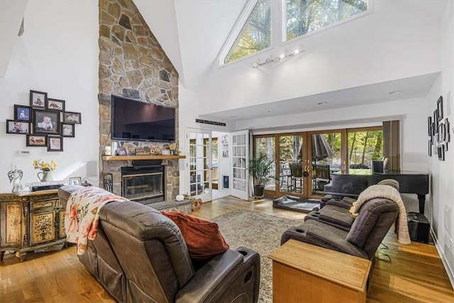 living room with light hardwood / wood-style floors, a fireplace, high vaulted ceiling, and french doors