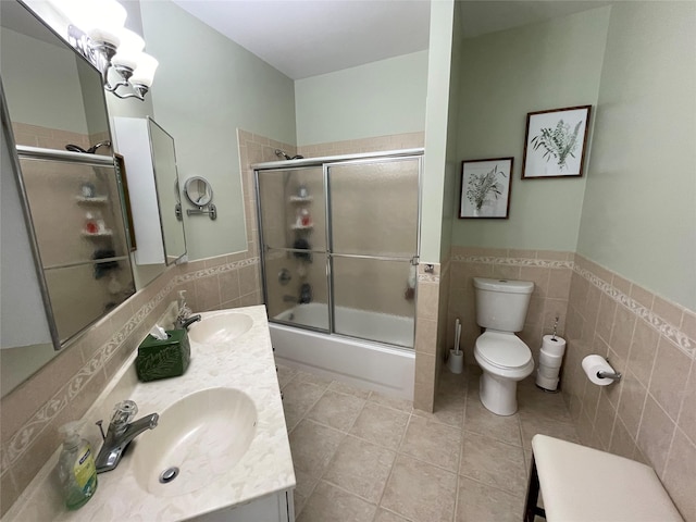 full bathroom featuring tile patterned floors, toilet, bath / shower combo with glass door, tile walls, and vanity