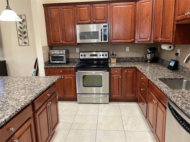 kitchen featuring stainless steel appliances, hanging light fixtures, sink, and dark stone counters