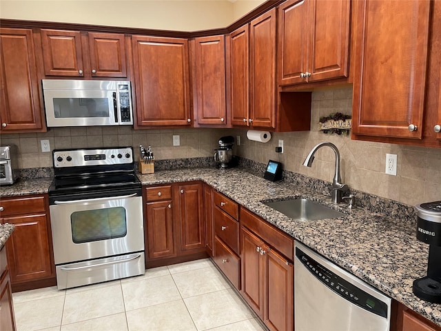 kitchen featuring sink, tasteful backsplash, light tile patterned floors, dark stone countertops, and stainless steel appliances