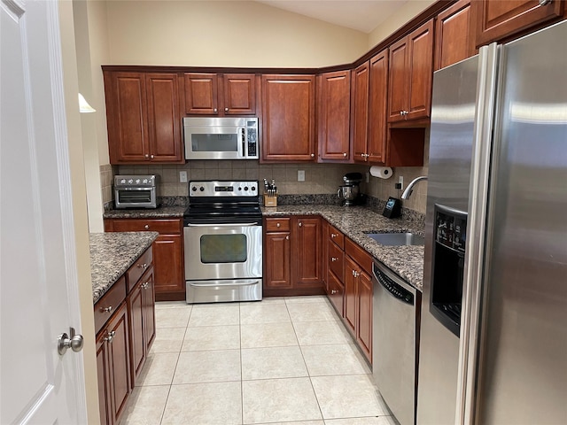 kitchen featuring sink, dark stone countertops, stainless steel appliances, tasteful backsplash, and light tile patterned flooring