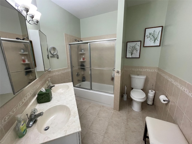 full bathroom featuring bath / shower combo with glass door, tile walls, vanity, toilet, and tile patterned floors