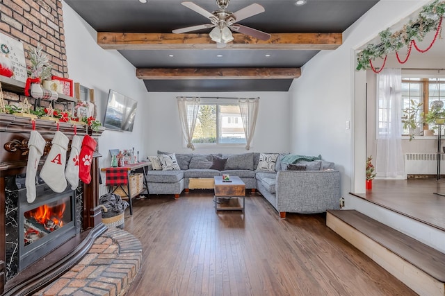 living room featuring hardwood / wood-style flooring, a brick fireplace, radiator, and beam ceiling