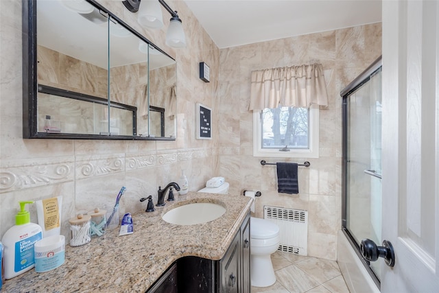 full bathroom with radiator heating unit, tile walls, enclosed tub / shower combo, vanity, and toilet