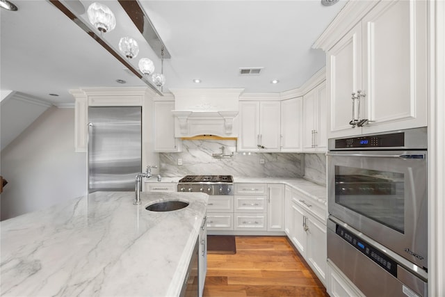 kitchen with premium range hood, sink, appliances with stainless steel finishes, light stone countertops, and white cabinets