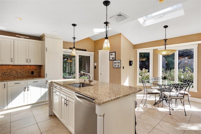 kitchen featuring sink, light stone counters, a center island with sink, stainless steel dishwasher, and vaulted ceiling with skylight