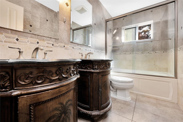 full bathroom with bath / shower combo with glass door, tile walls, tile patterned flooring, vanity, and toilet