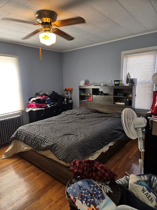 bedroom featuring hardwood / wood-style floors, crown molding, radiator heating unit, and ceiling fan