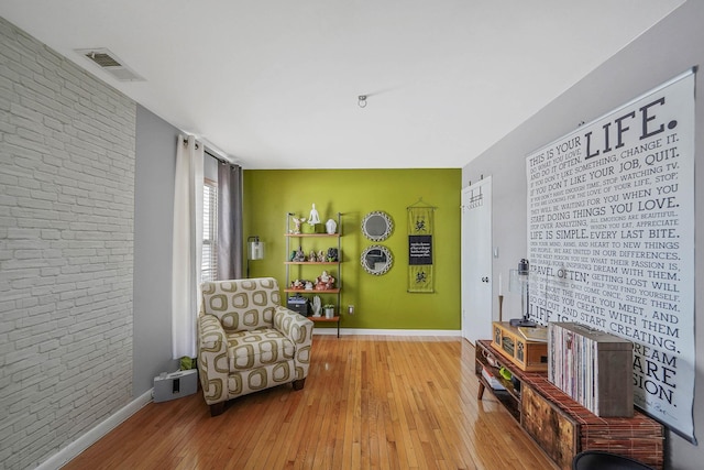 sitting room featuring brick wall and light hardwood / wood-style flooring