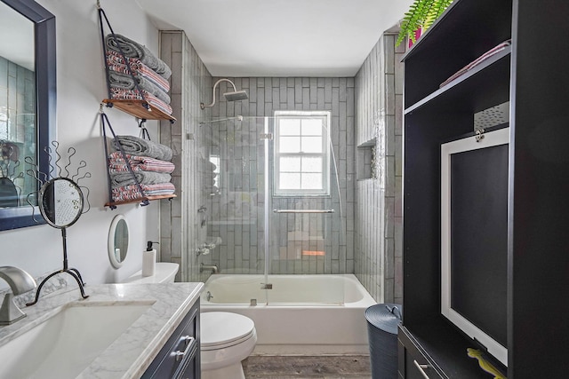 full bathroom featuring hardwood / wood-style flooring, enclosed tub / shower combo, vanity, and toilet