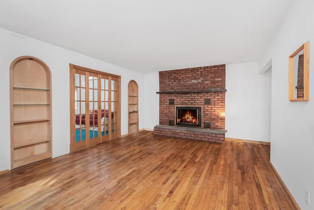 unfurnished living room with hardwood / wood-style flooring, a brick fireplace, and built in features