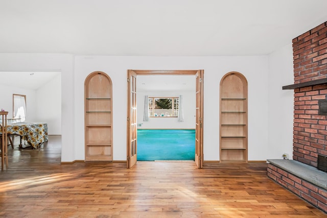 living room featuring wood-type flooring, a fireplace, and built in shelves