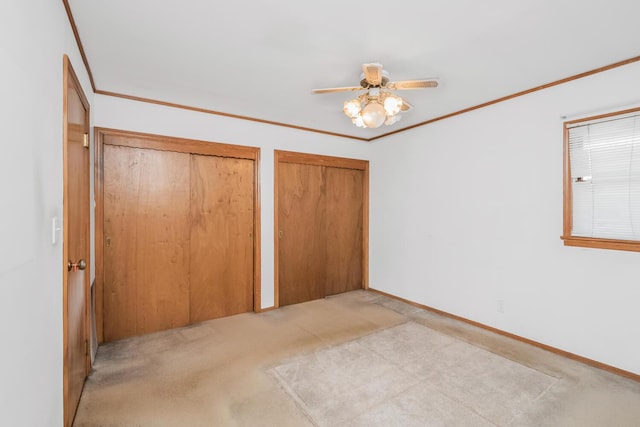 unfurnished bedroom featuring crown molding, two closets, light colored carpet, and ceiling fan