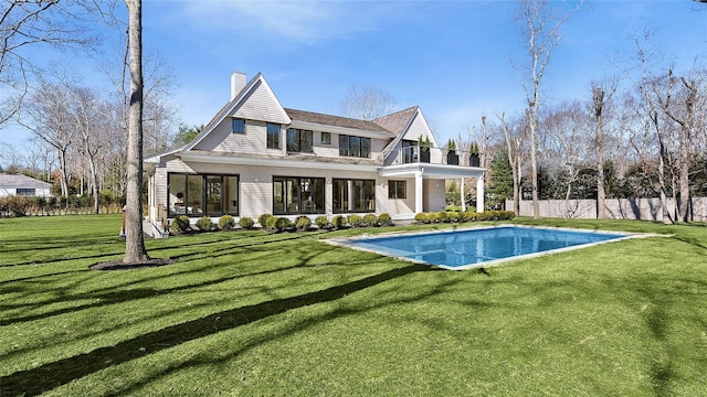 rear view of property with a fenced in pool, a balcony, and a yard