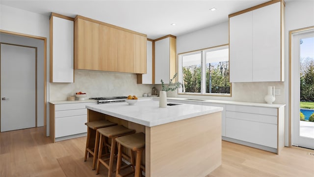 kitchen with white cabinetry, light wood-type flooring, tasteful backsplash, and a kitchen island