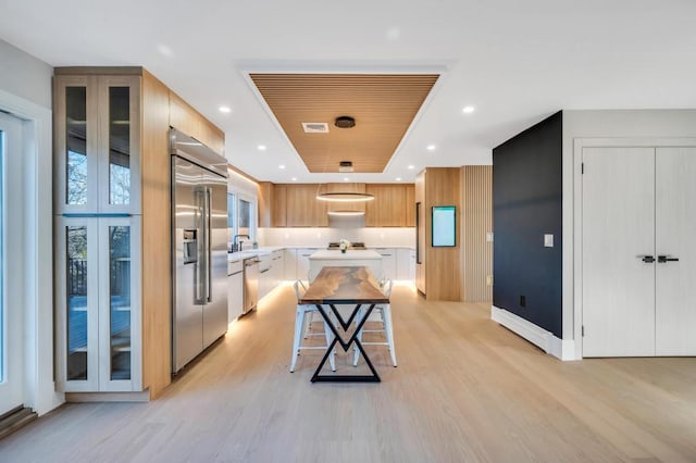 kitchen featuring appliances with stainless steel finishes, a kitchen island, a tray ceiling, a kitchen bar, and light wood-type flooring