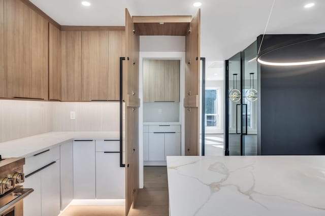 kitchen featuring stainless steel range oven, white cabinetry, light brown cabinets, light stone countertops, and light hardwood / wood-style floors