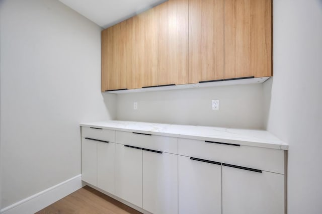 kitchen with white cabinetry, light brown cabinetry, light stone counters, and light wood-type flooring