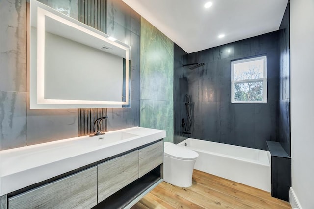 full bathroom featuring tile walls, vanity, wood-type flooring, toilet, and tiled shower / bath