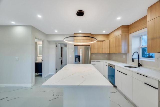 kitchen with sink, appliances with stainless steel finishes, white cabinetry, light stone countertops, and a kitchen island