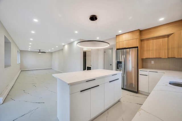 kitchen featuring a center island, stainless steel fridge, light stone countertops, and white cabinets