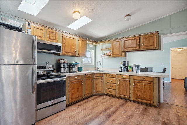 kitchen with sink, light hardwood / wood-style flooring, stainless steel appliances, vaulted ceiling with skylight, and kitchen peninsula