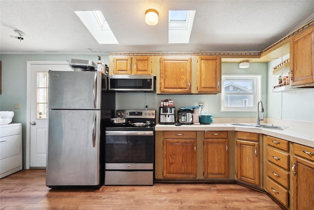 kitchen featuring washer / dryer, sink, light hardwood / wood-style flooring, a textured ceiling, and stainless steel appliances