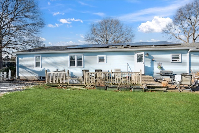 back of property featuring a wooden deck, a yard, and solar panels