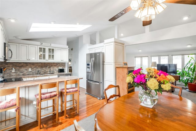 dining space with sink, light hardwood / wood-style flooring, vaulted ceiling with skylight, and ceiling fan