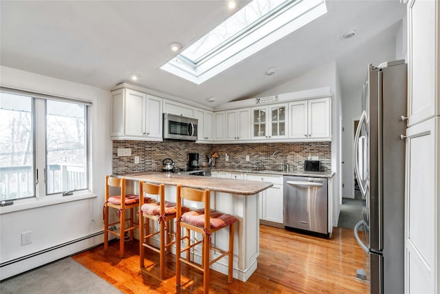 kitchen featuring appliances with stainless steel finishes, a kitchen breakfast bar, kitchen peninsula, vaulted ceiling with skylight, and white cabinets