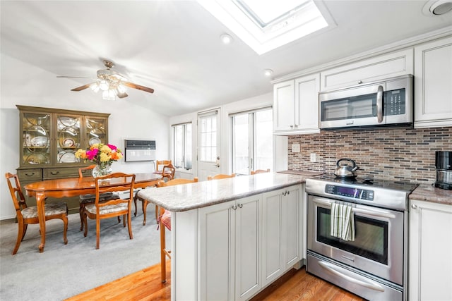 kitchen featuring stainless steel appliances, lofted ceiling with skylight, white cabinetry, and kitchen peninsula