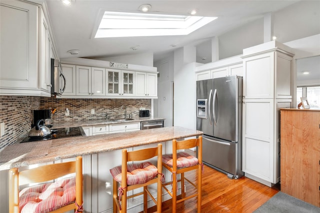 kitchen with sink, appliances with stainless steel finishes, white cabinetry, lofted ceiling with skylight, and kitchen peninsula