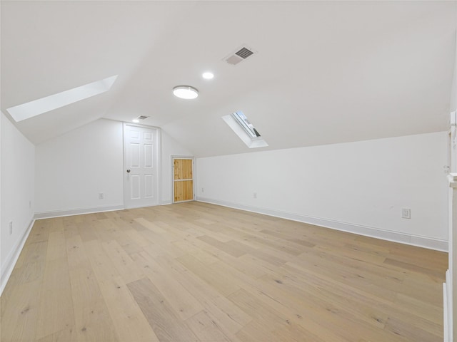 additional living space with lofted ceiling with skylight and light hardwood / wood-style flooring