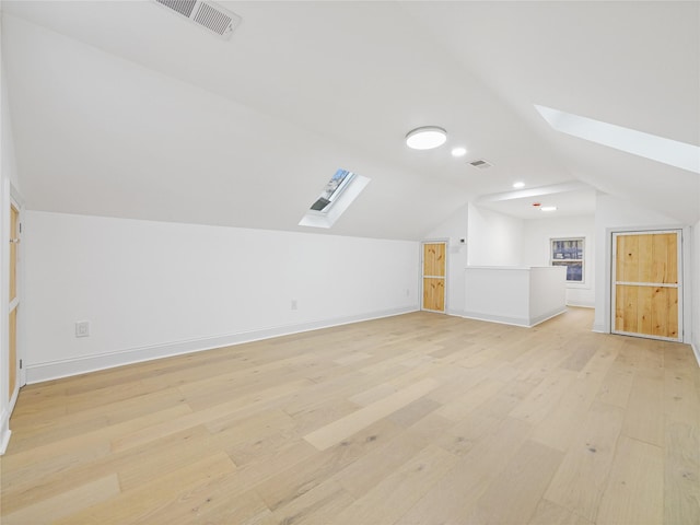 additional living space featuring light hardwood / wood-style flooring and lofted ceiling with skylight