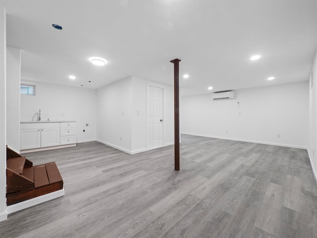 basement featuring a wall mounted air conditioner, sink, and light hardwood / wood-style floors