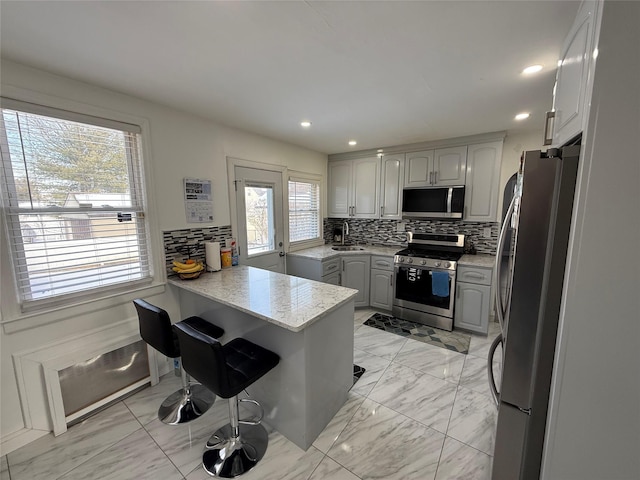 kitchen featuring sink, gray cabinets, stainless steel appliances, decorative backsplash, and kitchen peninsula