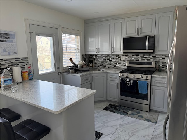 kitchen with appliances with stainless steel finishes, kitchen peninsula, sink, and light stone countertops