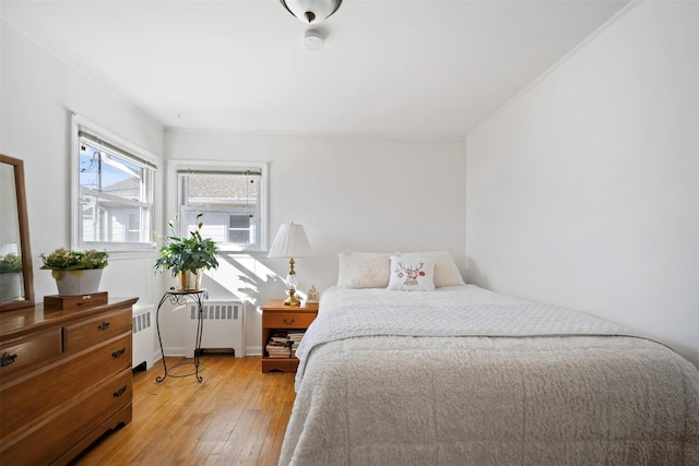 bedroom with crown molding, radiator, and light wood-type flooring