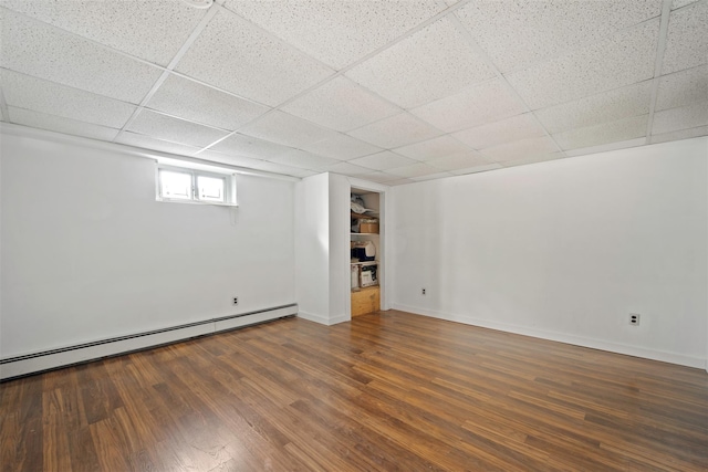 basement featuring dark wood-type flooring, a paneled ceiling, and a baseboard heating unit